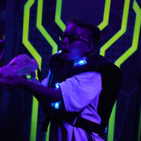 Smiling guest aiming a laser tag blaster in the blacklight arena at The Fun Lab in Blaine, MN
